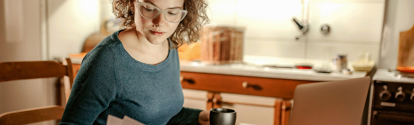 A woman holding a cup of coffee in one hand and her energy bill in the other.