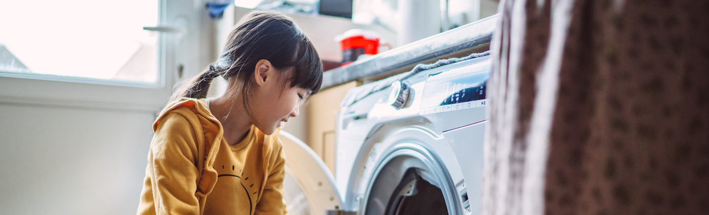 A smiling child standing in front of a washing machine in a brightly lit room.