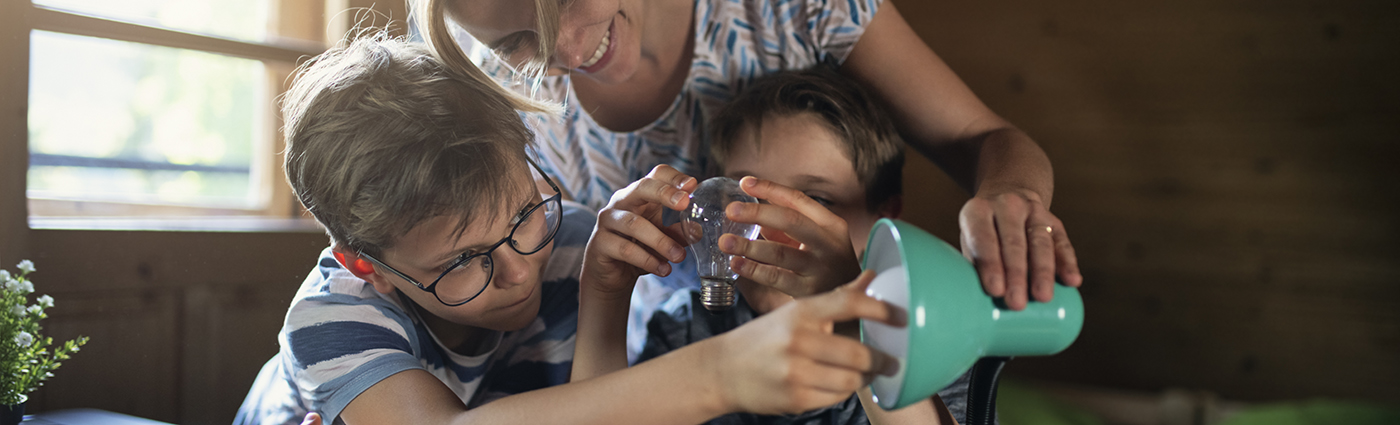 A mother smiling and hugging her two kids while holding a lightbulb in front of them.