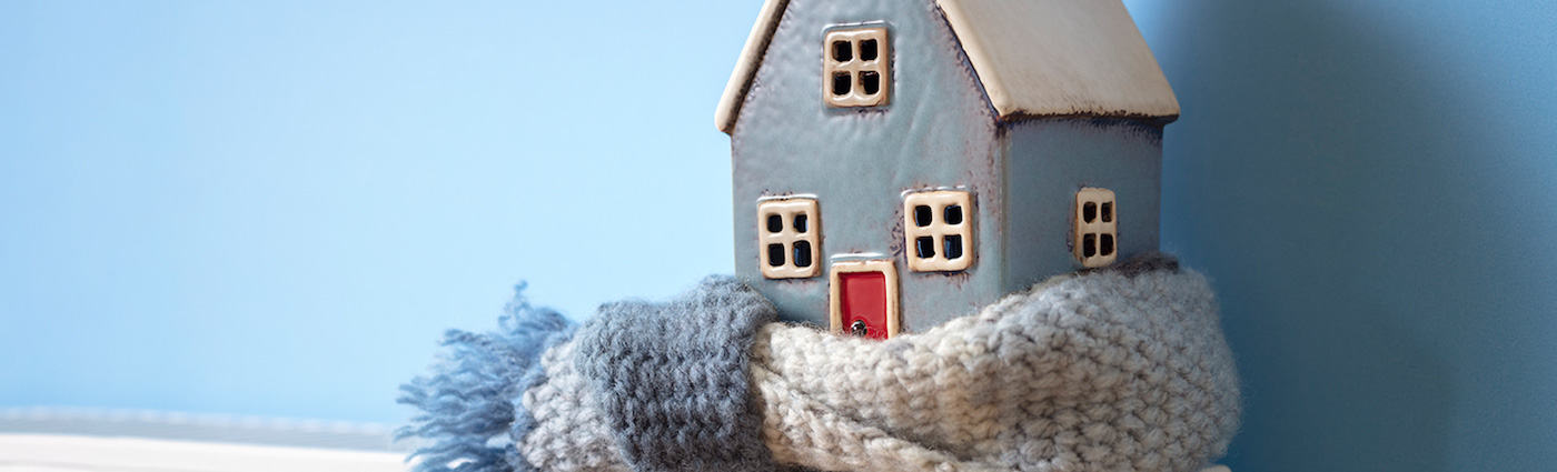 A model of a blue house with a red door wrapped by a white wool scarf.