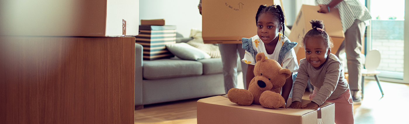 Two children helping their parents unpack the cardboard boxes in a living room.
